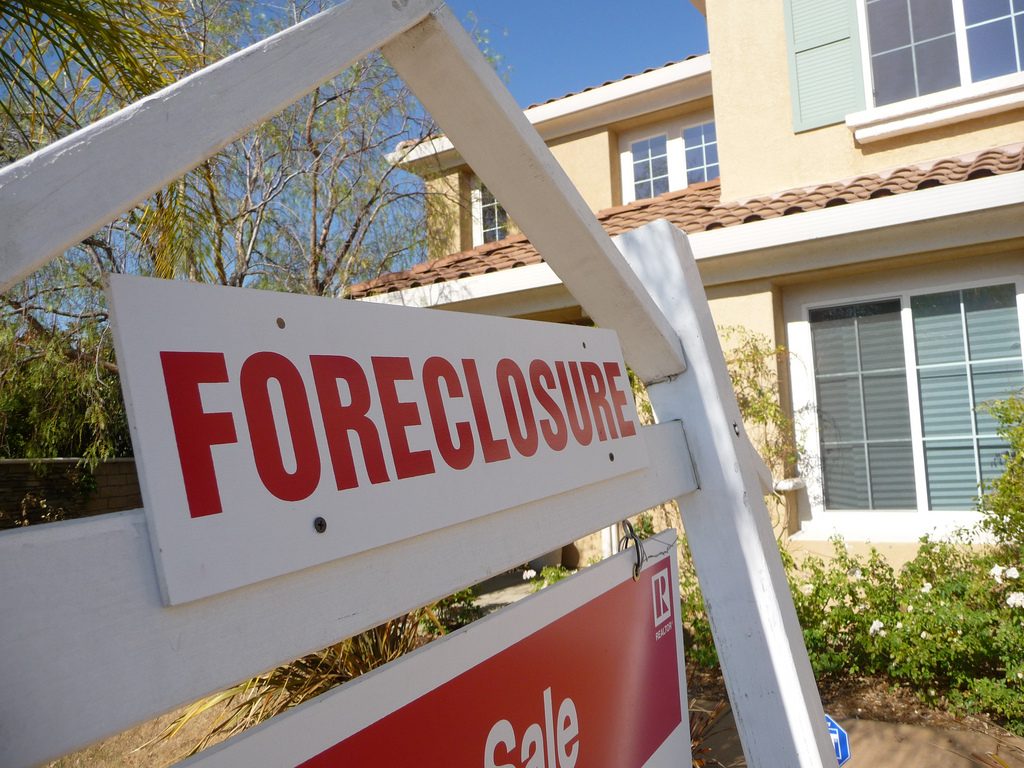 real estate sign that says foreclosure in front of house. short sale and foreclosure